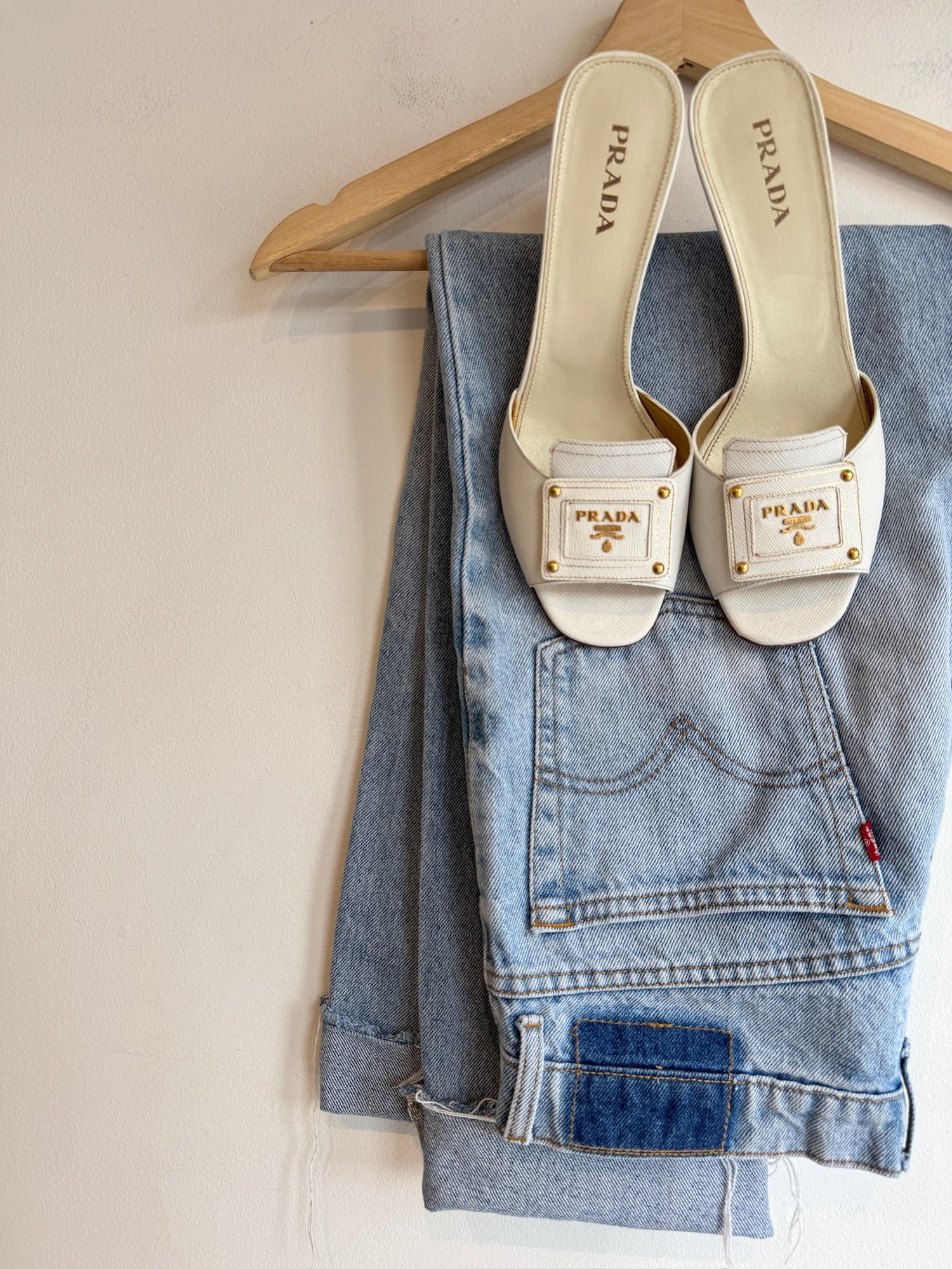 Cream Prada slide sandals with gold hardware resting on light-wash jeans
